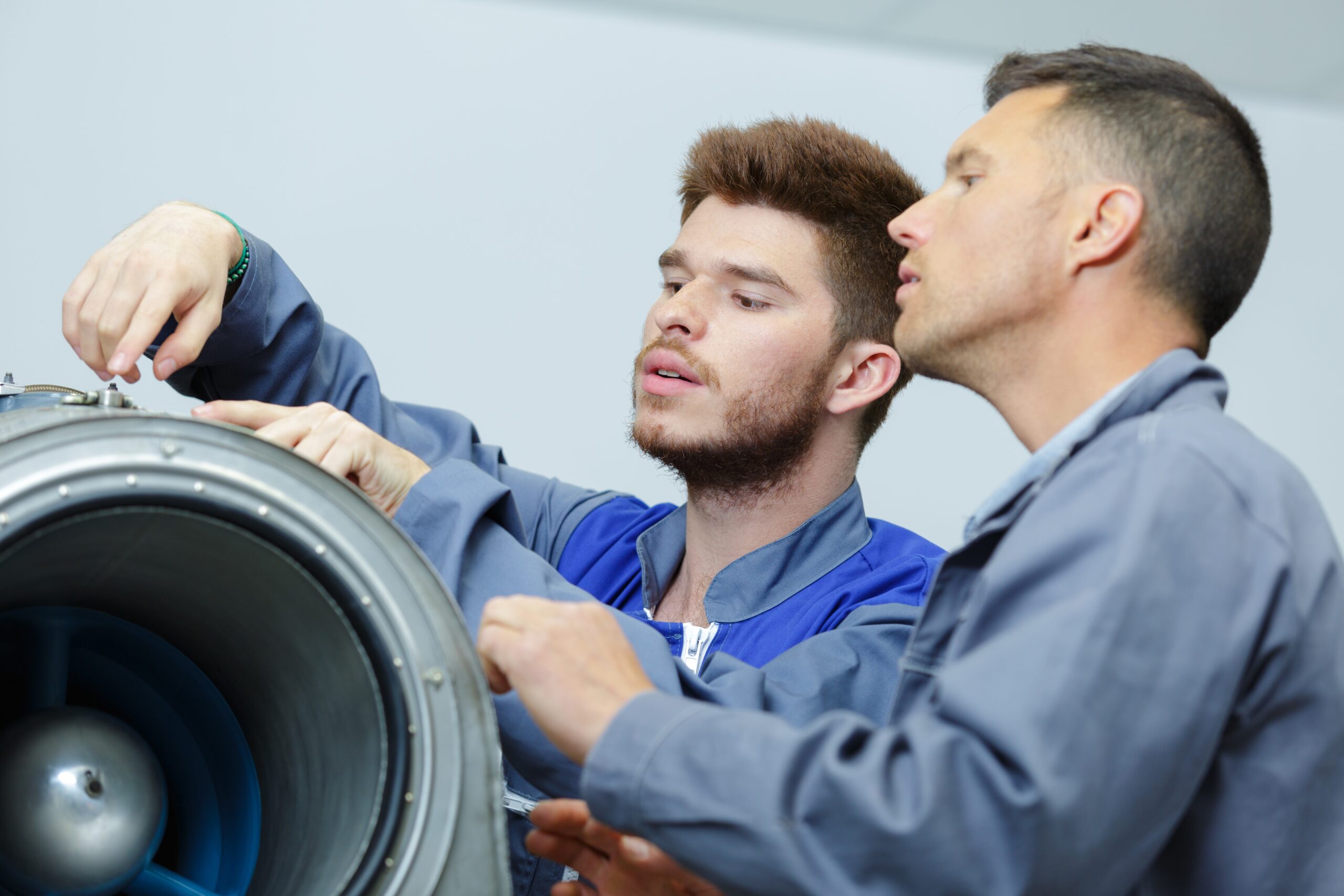 Deux hommes blancs, un plus jeune et un plus agé, en observation d'un boulon sur un réacteur d'avion