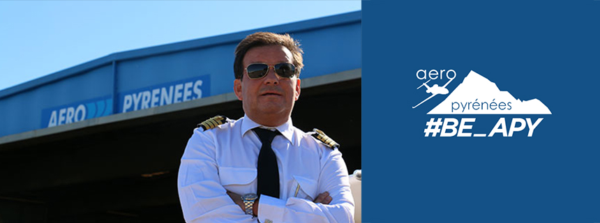 Un pilote posant devant un hangar à avion portant le logo d'Aéropyrénées.